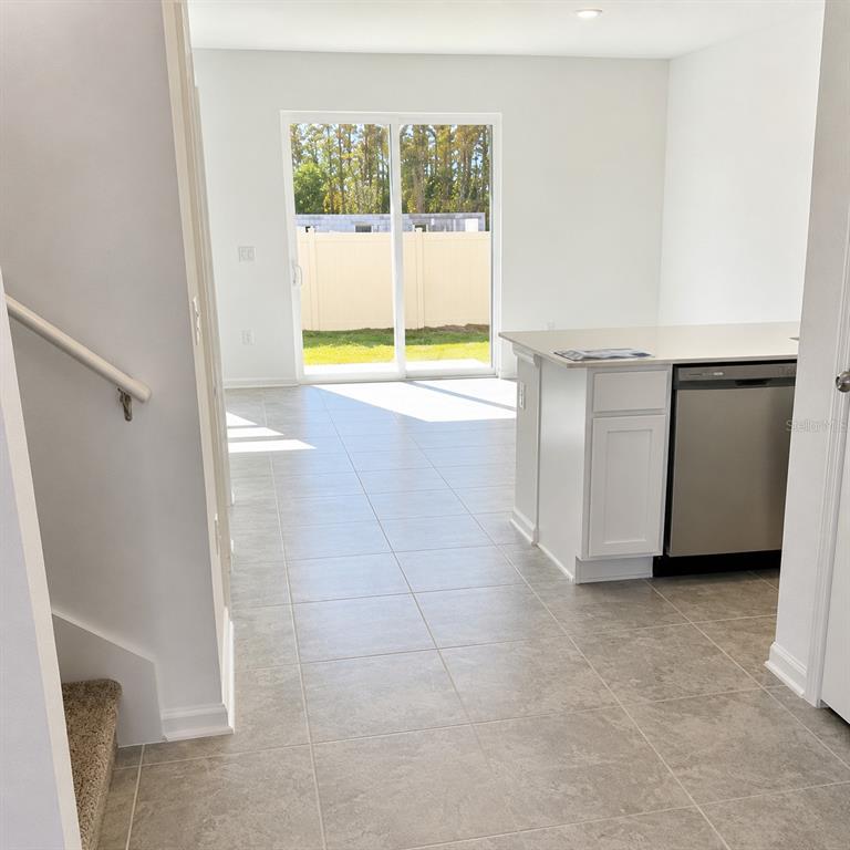 A kitchen with a stainless steel dishwasher and tile flooring leads to a sliding glass door — 2528 SKYLINE LOOP, KISSIMMEE, FL