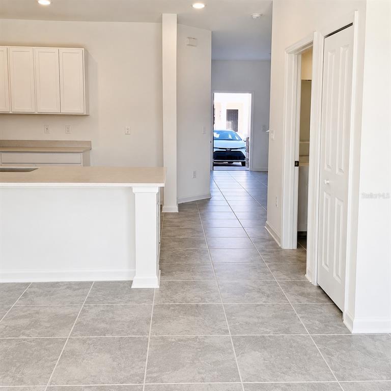 A kitchen with white cabinets and a tile floor leads to a hallway and garage — 2528 SKYLINE LOOP, KISSIMMEE, FL