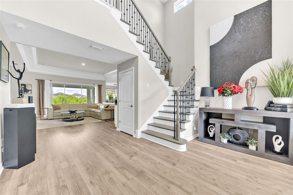 A bright foyer features light wood flooring, a staircase with iron railings, and a console table — 7201 TALAMORE DRIVE, WESLEY CHAPEL, FL