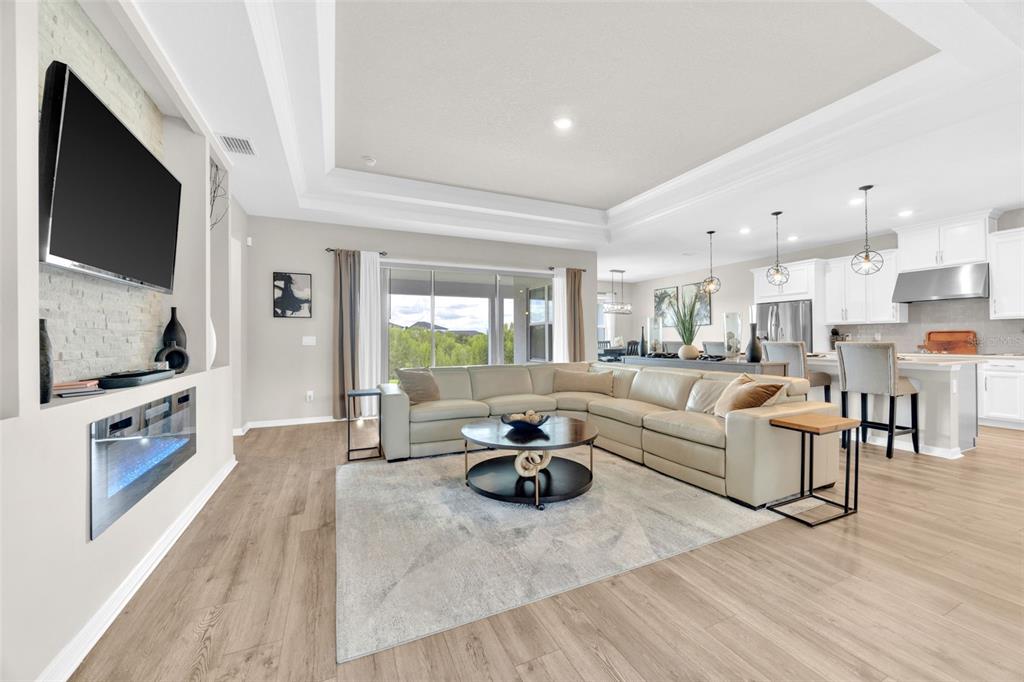 A spacious open-concept living room features a sectional sofa, fireplace, and an adjacent kitchen — 7201 TALAMORE DRIVE, WESLEY CHAPEL, FL