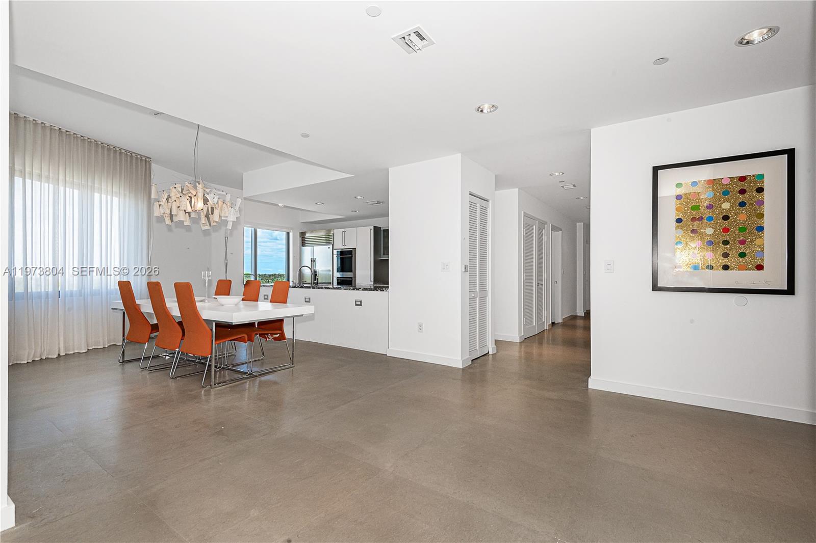 A dining area with orange chairs and a modern chandelier sits adjacent to a kitchen — 6101 Aqua Ave # 702, Miami Beach FL 33141, MIAMI BEACH, FL