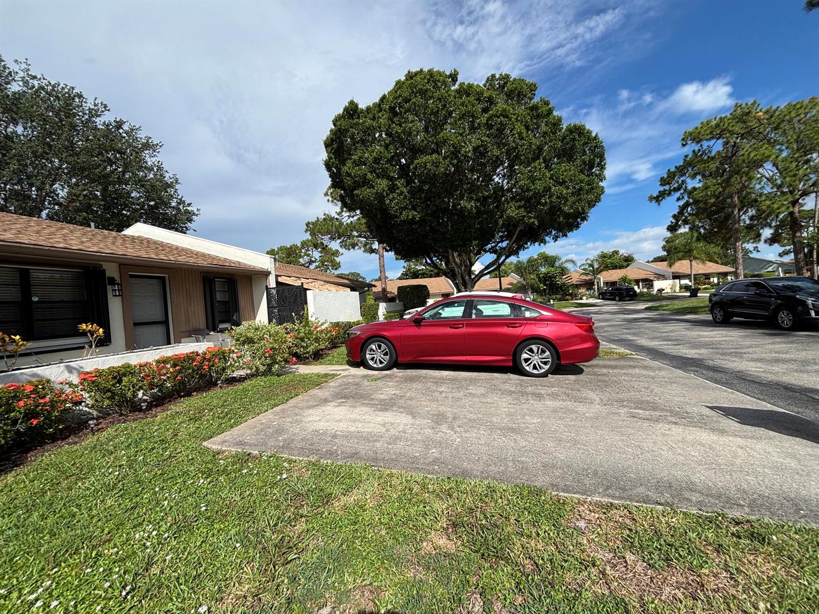 A red sedan is parked in the concrete driveway of a single-story house with landscaping — 6132 Fairfield Circle # 7, FL 33463, FL