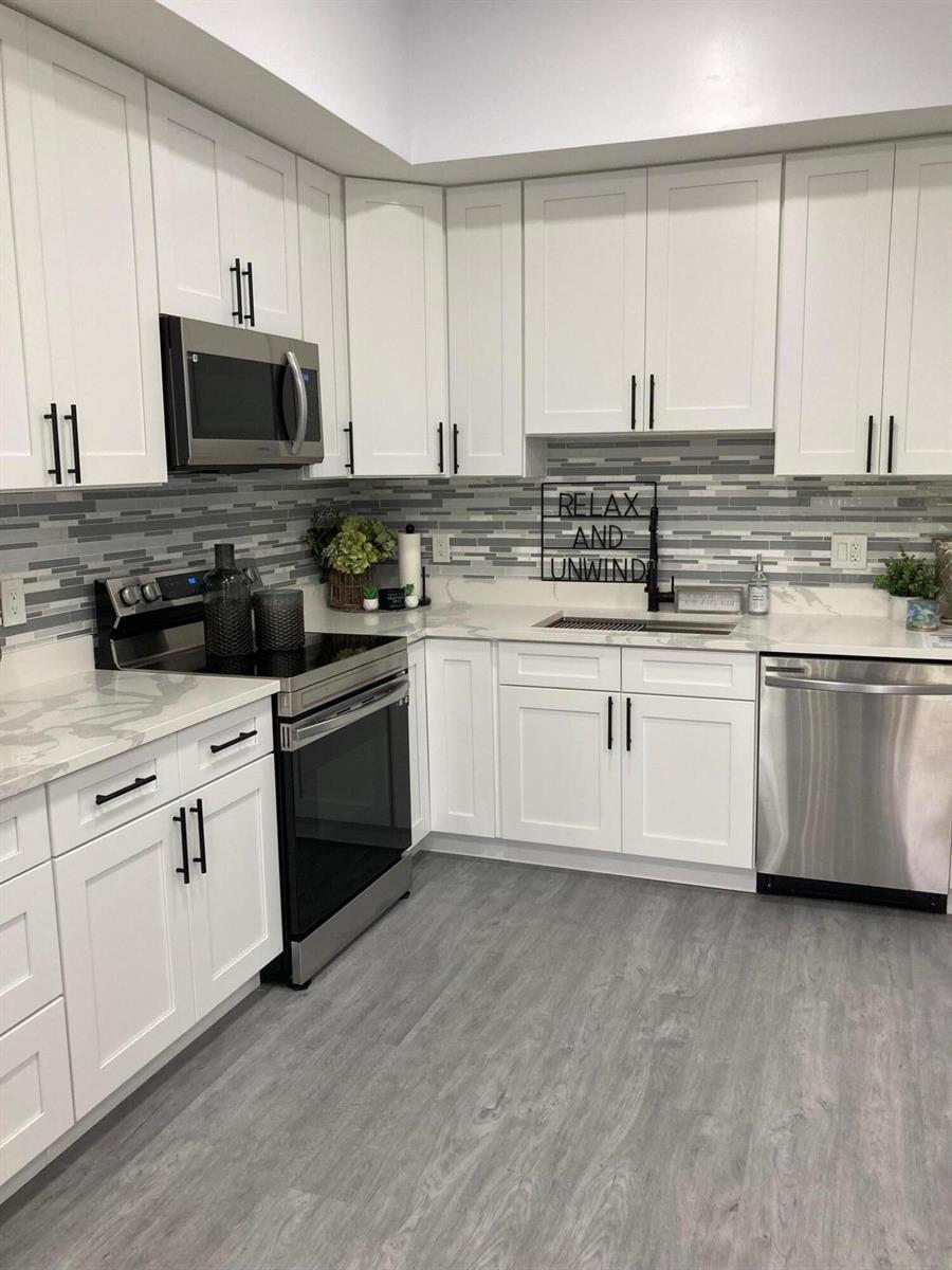 A kitchen features white cabinets, stainless steel appliances, a gray tiled backsplash, and light countertops — 6132 Fairfield Circle # 7, FL 33463, FL