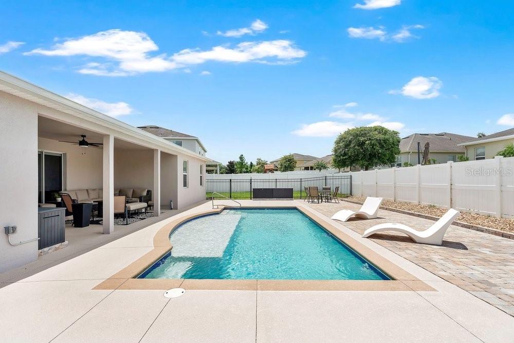 A backyard features a swimming pool with a tanning ledge, a covered patio, and lounge chairs — 1086 ROCK CREEK STREET, APOPKA, FL