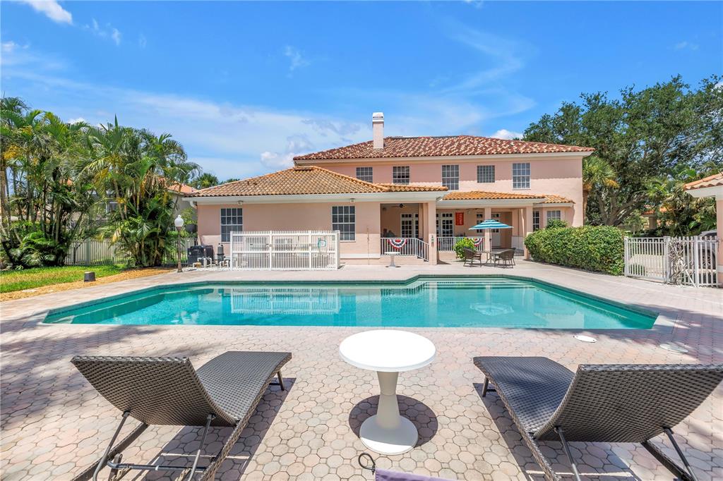 A backyard swimming pool sits in front of a two-story peach-colored house with a patio — 4930 SANDPIPER LANE S, ST PETERSBURG, FL