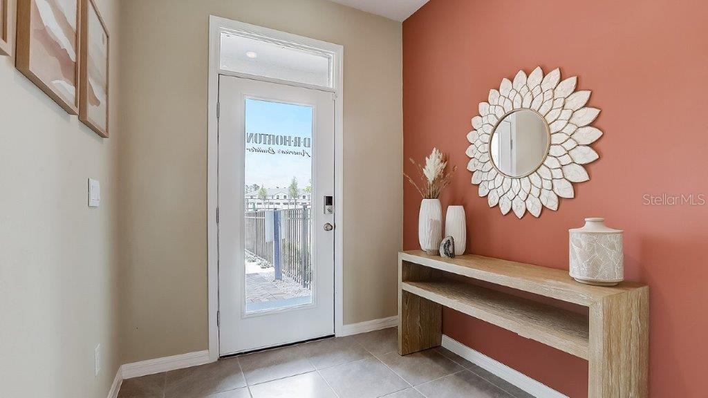 An entryway features a white front door, a wooden console table, and a terracotta-colored wall — 32611 MIDSUMMER NIGHT LANE, WESLEY CHAPEL, FL