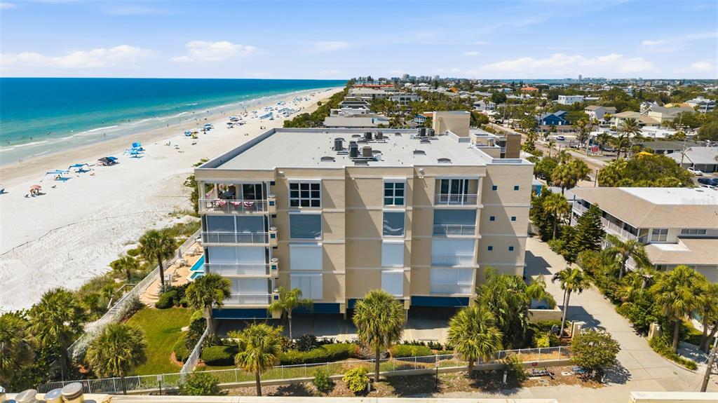 An aerial view shows a multi-story tan apartment building situated next to a sandy beach — 2 15TH AVENUE UNIT 401, INDIAN ROCKS BEACH, FL