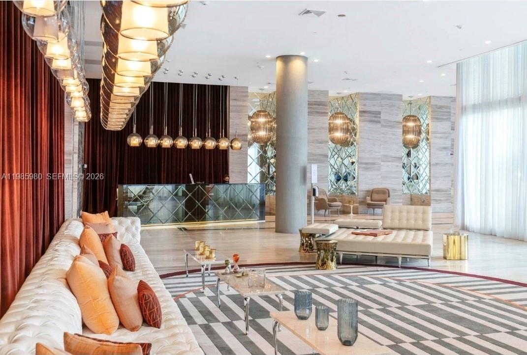 A modern hotel lobby features a tufted sofa, geometric rug, and a long reception desk — 2000 Metropica Way # 2507, Sunrise FL 33323, SUNRISE, FL