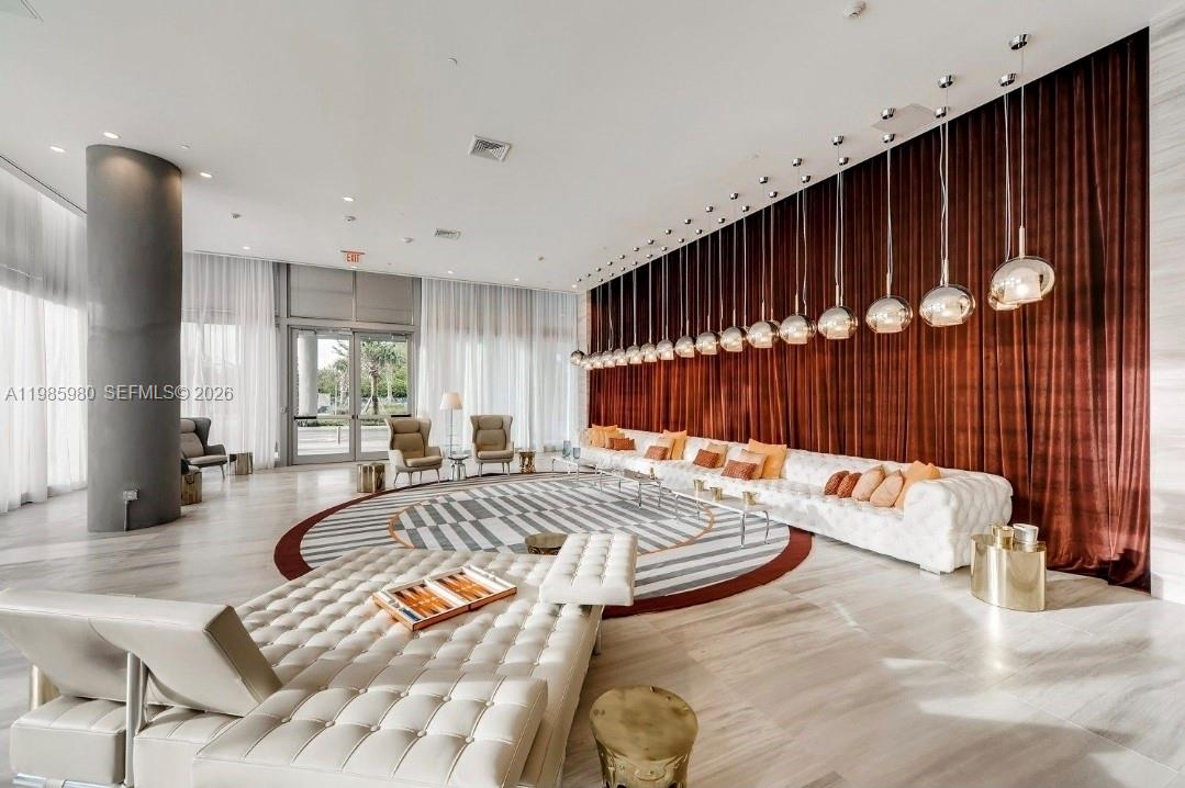 A modern, spacious lobby features a long white tufted sofa, pendant lighting, and floor-to-ceiling curtains — 2000 Metropica Way # 2507, Sunrise FL 33323, SUNRISE, FL