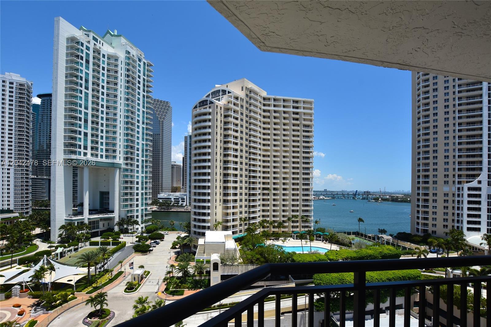A balcony view overlooks a swimming pool, lush landscaping, and high-rise buildings near the water — 540 Brickell Key Dr # 1513, Miami FL 33131, MIAMI, FL