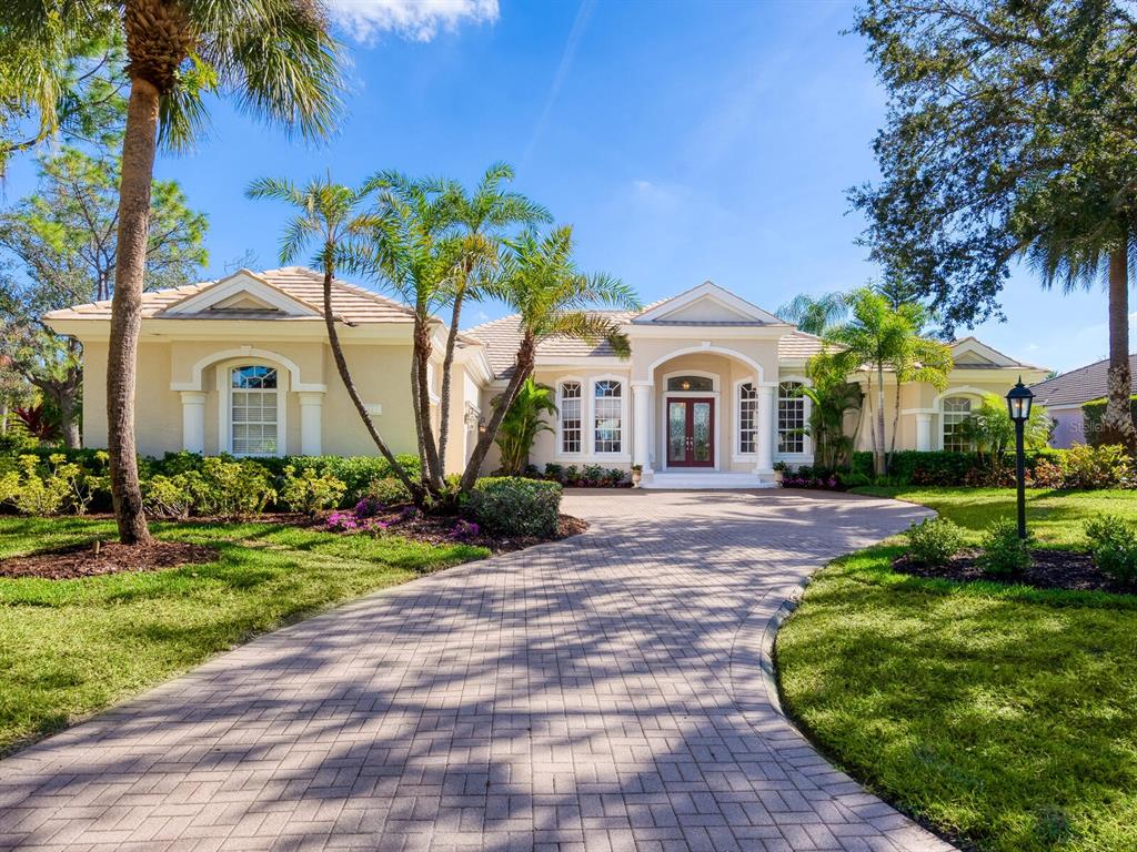 A single-story house with a paved driveway, palm trees, and a central arched entryway — 7311 WESTMINSTER COURT, UNIVERSITY PARK, FL