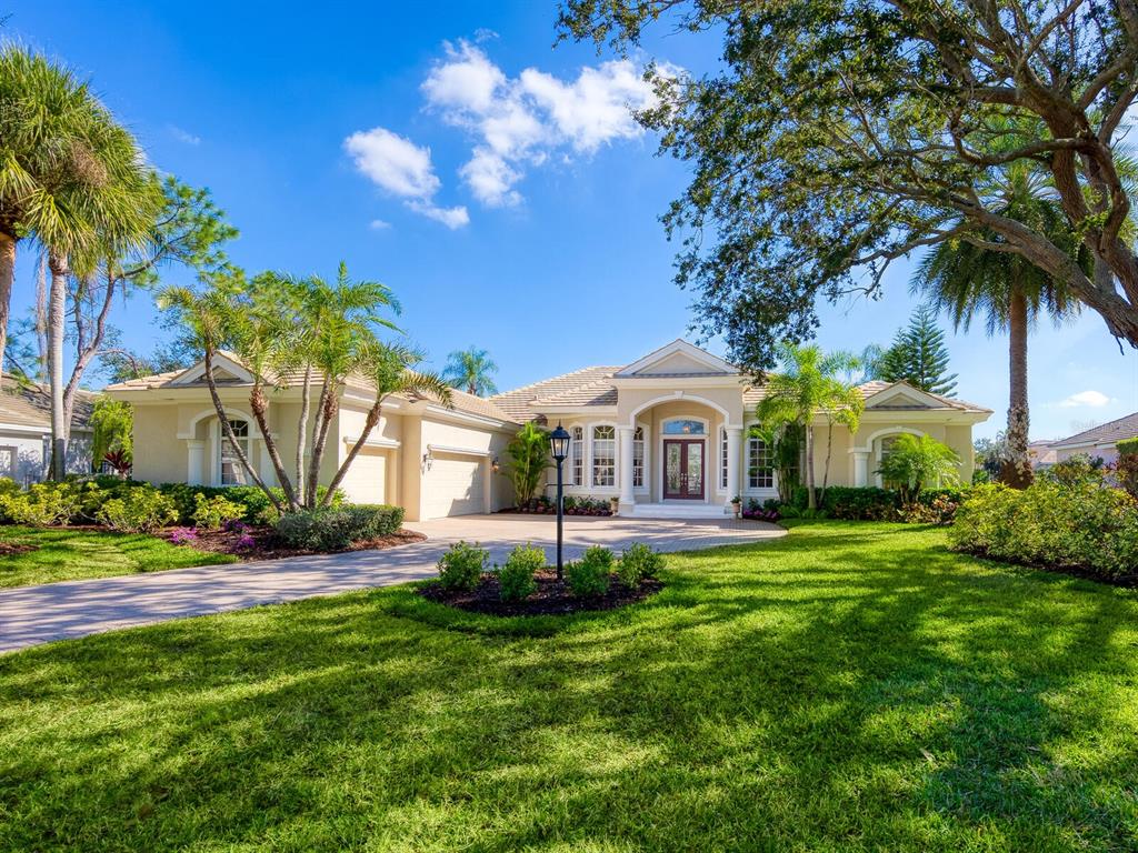 A single-story suburban house with a beige exterior, a paved driveway, and lush landscaping — 7311 WESTMINSTER COURT, UNIVERSITY PARK, FL