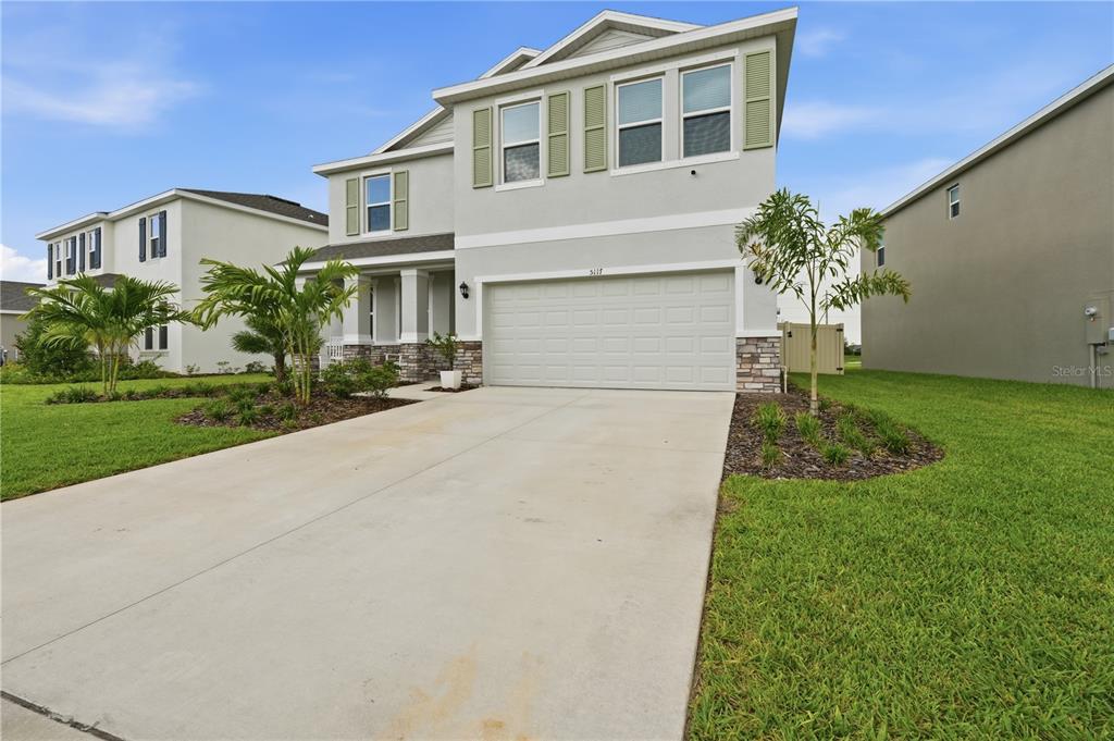 A two-story suburban house with a concrete driveway, stone accents, and green shutters — 5117 ROSADO RUN, BRADENTON, FL