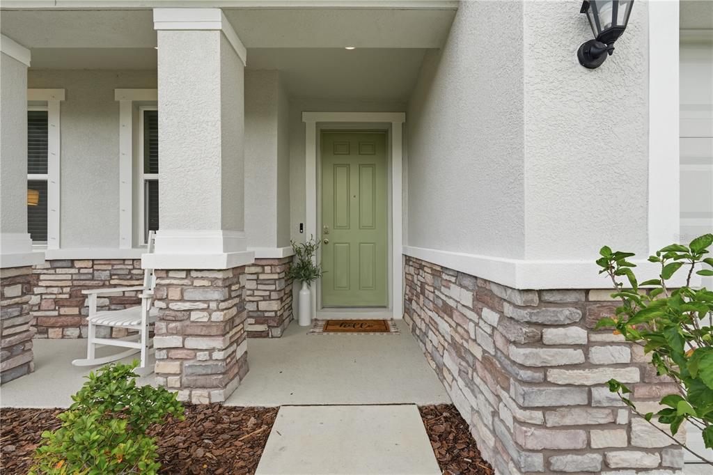 A covered front porch features a sage green door, stone veneer siding, and a rocking chair — 5117 ROSADO RUN, BRADENTON, FL