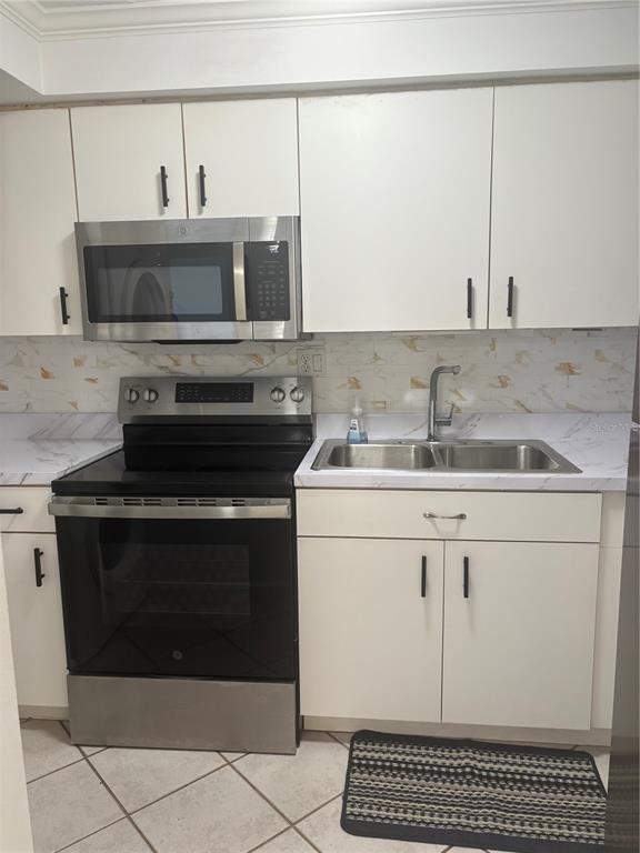 A kitchen features white cabinets, stainless steel appliances, a marble-patterned backsplash, and tiled flooring — 503 ALBEE FARM ROAD UNIT B28, VENICE, FL