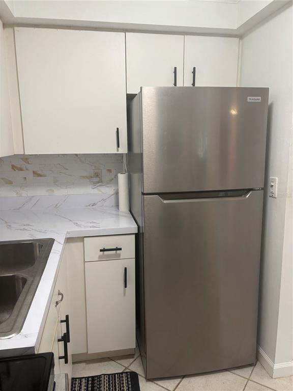 A kitchen features white cabinets, a stainless steel refrigerator, and a marble-patterned countertop — 503 ALBEE FARM ROAD UNIT B28, VENICE, FL