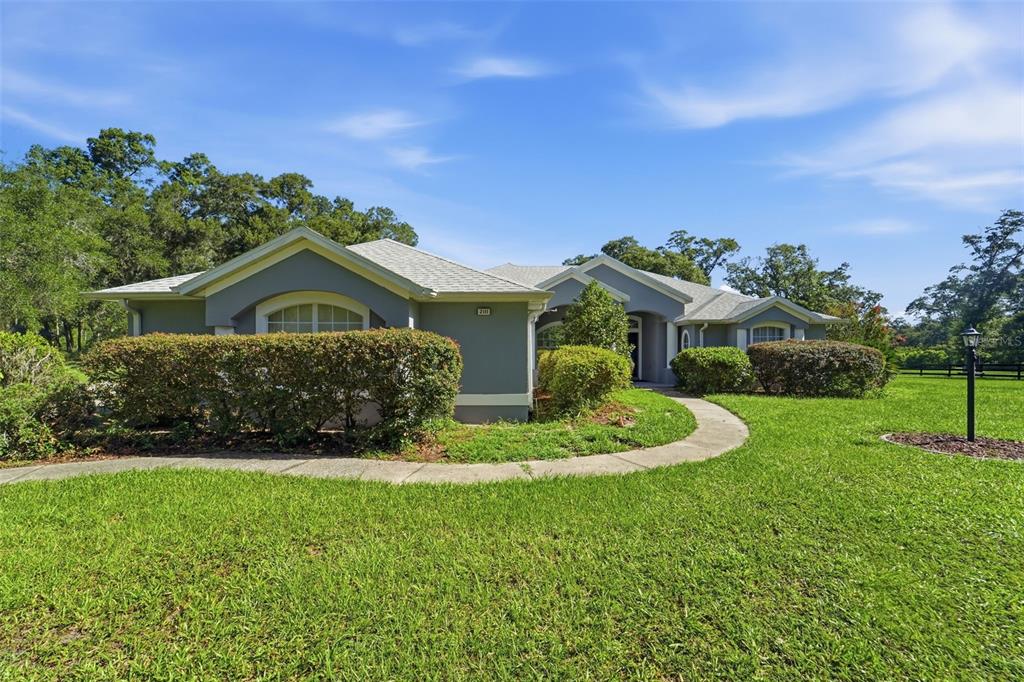 A single-story house with gray stucco siding and a curved walkway through the lawn — 2111 SUN VALLEY LANE, DELAND, FL