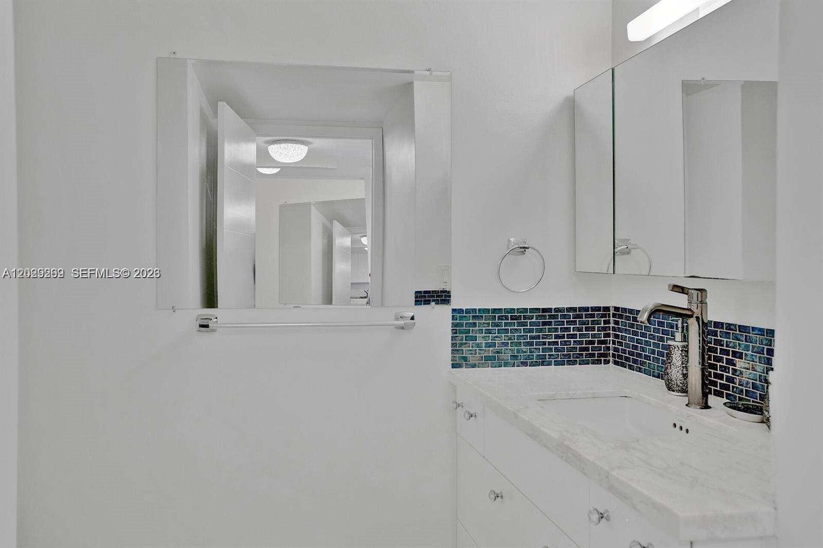 A bathroom features a white vanity with a marble countertop and blue tiled backsplash — 2500 Parkview Dr # 1008, Hallandale Beach FL 33009, HALLANDALE BEACH, FL