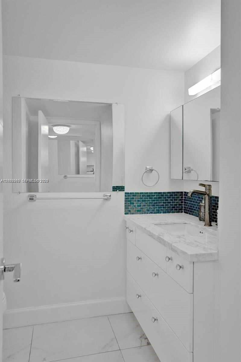 A bathroom features a white vanity with a marble countertop and a teal tiled backsplash — 2500 Parkview Dr # 1008, Hallandale Beach FL 33009, HALLANDALE BEACH, FL