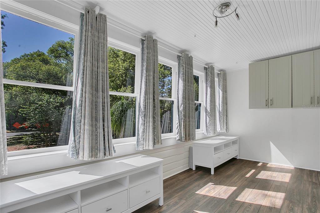 A sunroom with white walls, wood-look flooring, large windows with curtains, and white storage cabinets — 1209 S MYRTLE AVENUE UNIT A, SANFORD, FL
