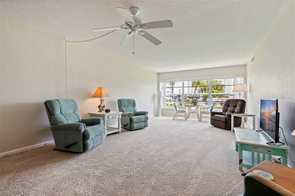 A carpeted living area features a glass-topped table, two chairs, and a view of a pool — 6363 GULF WINDS DRIVE UNIT 131, ST PETE BEACH, FL