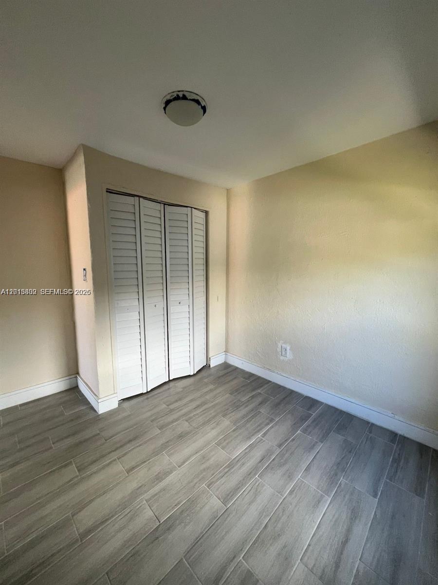 A small room features light-colored walls, wood-look tile flooring, and a white bi-fold closet door — 613 NW 15th Ave, Pompano Beach FL 33069, POMPANO BEACH, FL