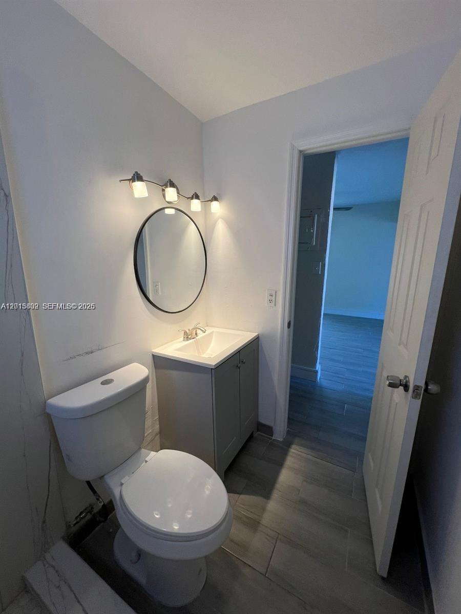 A small bathroom features a white toilet, a grey vanity with a sink, and a mirror — 613 NW 15th Ave, Pompano Beach FL 33069, POMPANO BEACH, FL