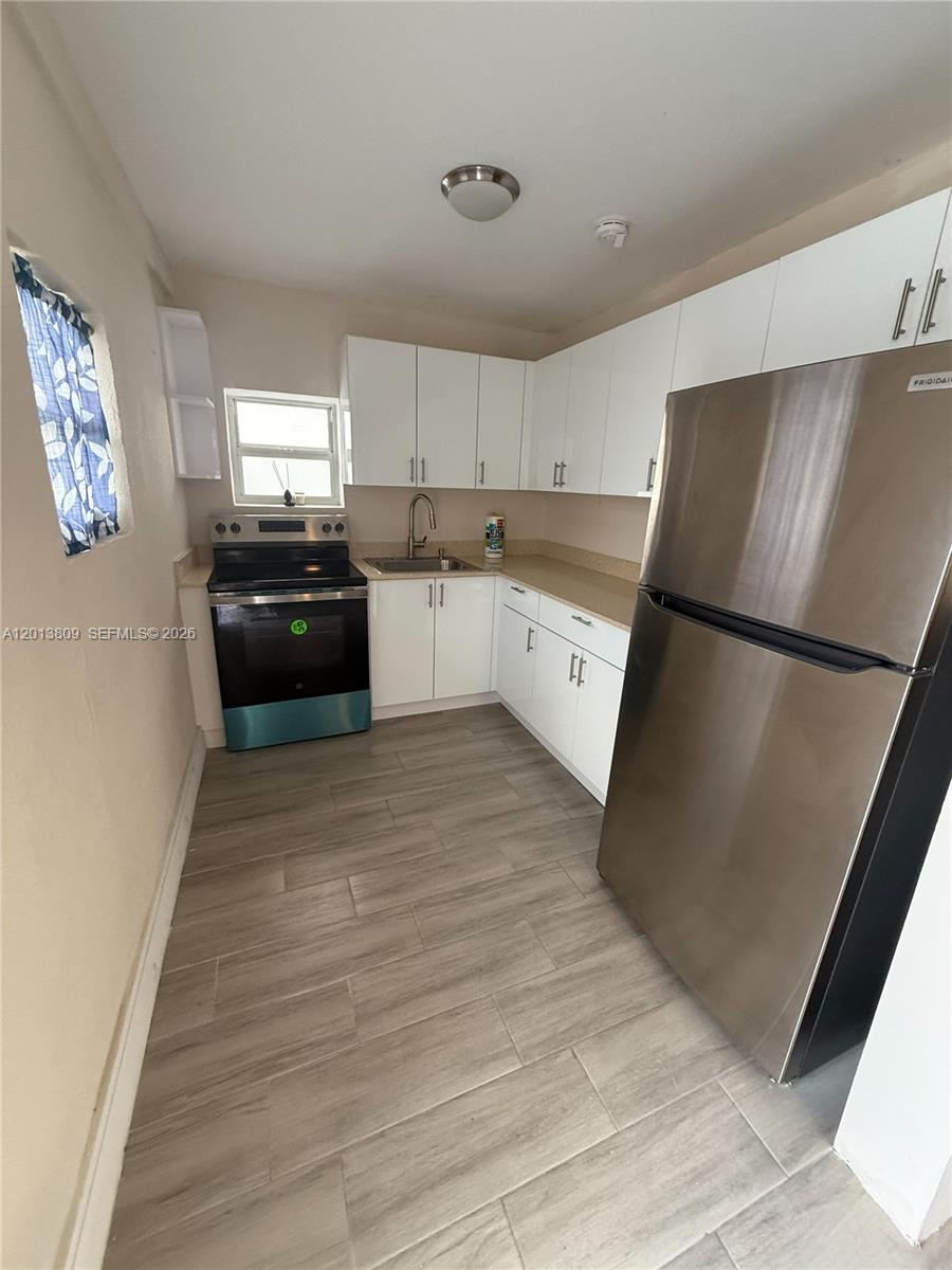 A small kitchen features white cabinets, stainless steel appliances, and light-colored wood-look tile flooring — 613 NW 15th Ave, Pompano Beach FL 33069, POMPANO BEACH, FL