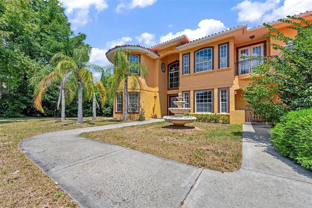 A two-story yellow stucco house features a front fountain, palm trees, and a concrete walkway — 13161 LAKE BUTLER BOULEVARD, WINDERMERE, FL