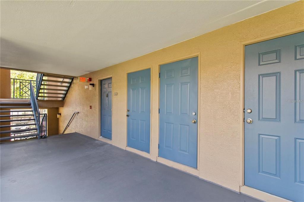 An exterior walkway features three blue doors and a metal staircase leading to another level — 7330 WESTPOINTE BOULEVARD UNIT 421, ORLANDO, FL