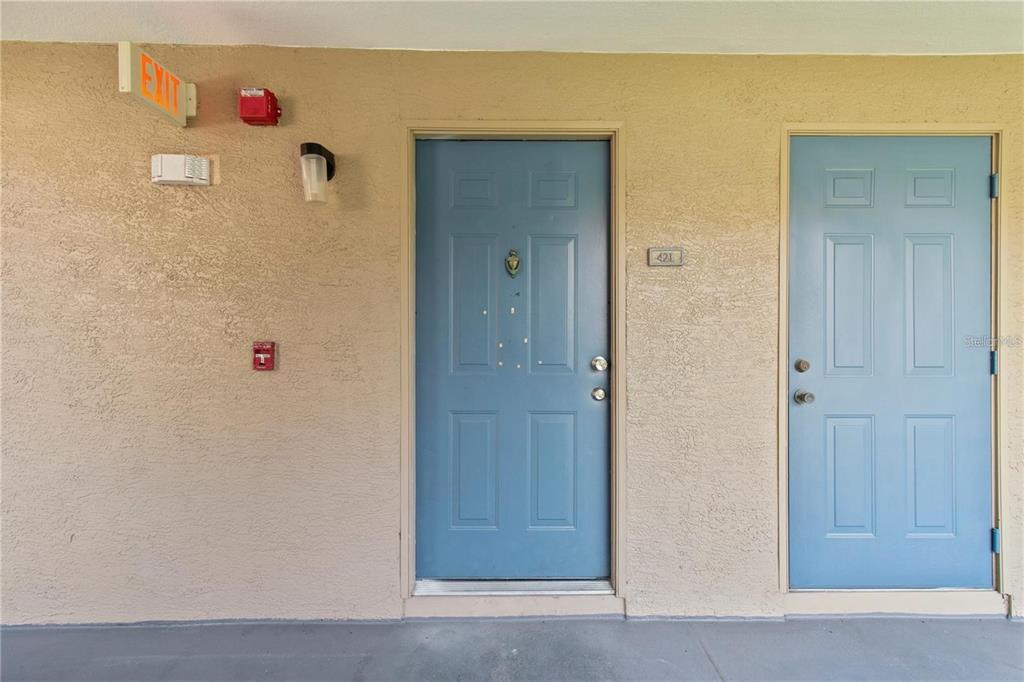 Two blue entry doors are set into a beige stucco wall with an exit sign — 7330 WESTPOINTE BOULEVARD UNIT 421, ORLANDO, FL