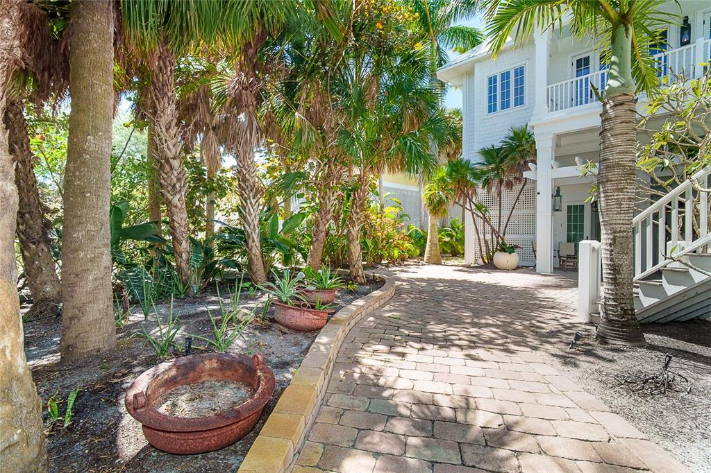 A brick paver walkway leads past palm trees and potted plants toward a white house — 7320 PALM ISLAND DRIVE, PLACIDA, FL