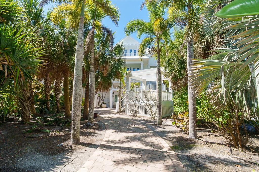 A stone pathway leads through palm trees toward a multi-story white house with a porch — 7320 PALM ISLAND DRIVE, PLACIDA, FL