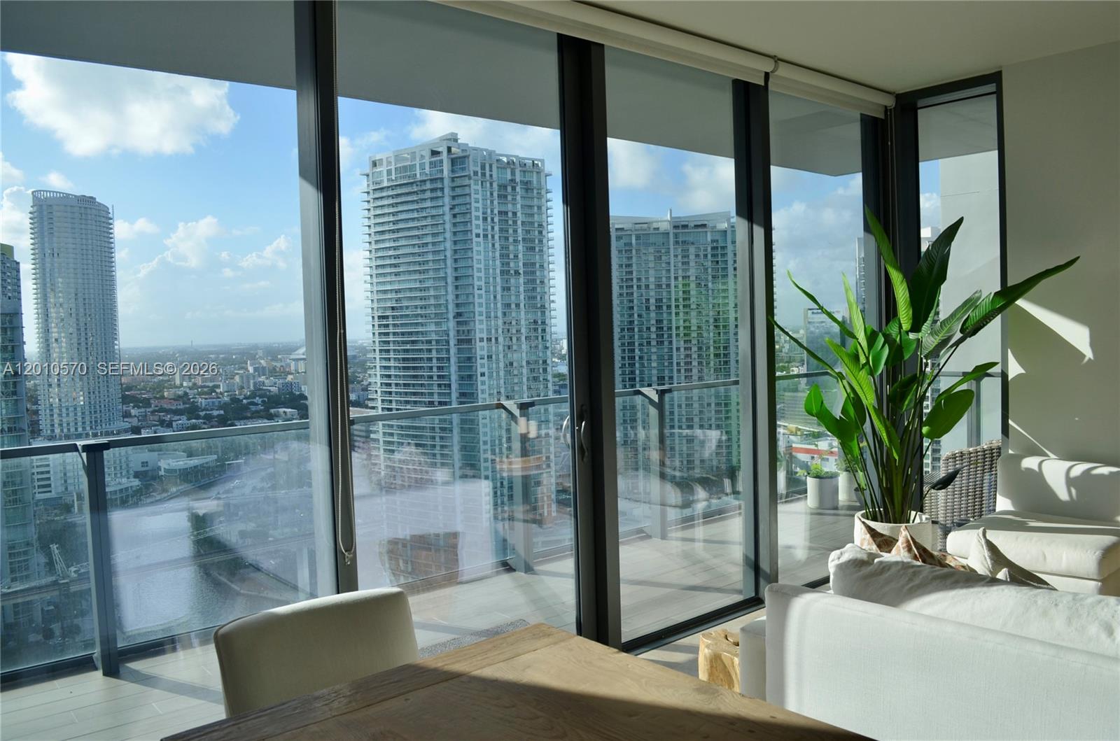 A modern living room features floor-to-ceiling windows overlooking a city skyline and a balcony — 68 SE 6th St # 2708, Miami FL 33131, MIAMI, FL