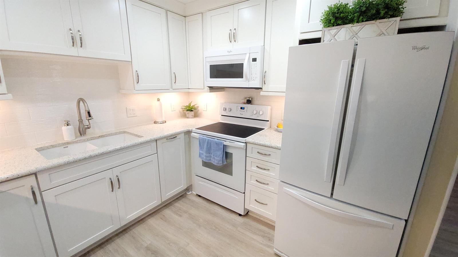 A white kitchen features shaker cabinets, a speckled countertop, and stainless steel appliances — 34 Somerset B, West Palm Beach FL 33417, WEST PALM BEACH, FL