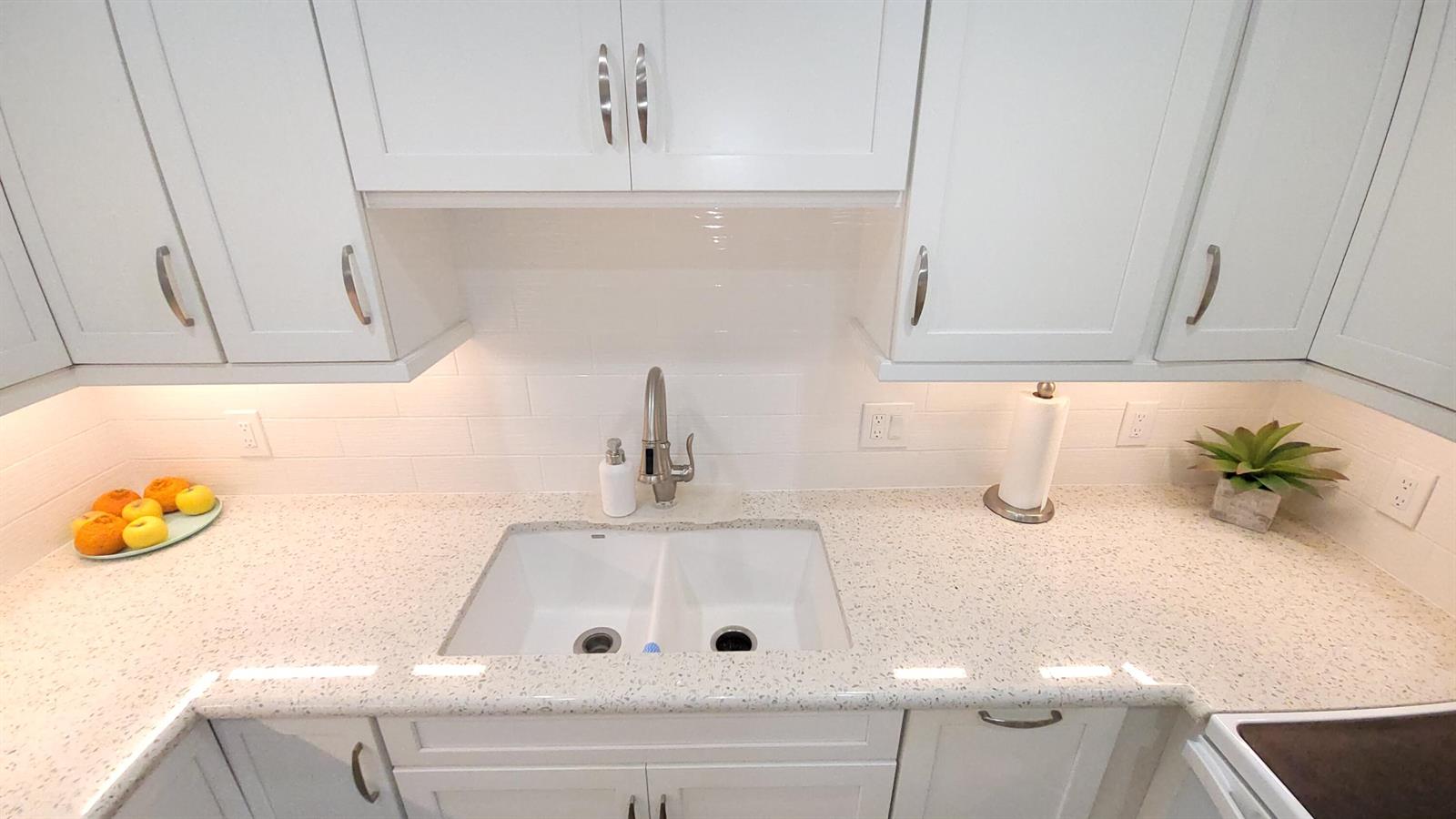 A kitchen features white cabinets, a speckled countertop, a double sink, and under-cabinet lighting — 34 Somerset B, West Palm Beach FL 33417, WEST PALM BEACH, FL