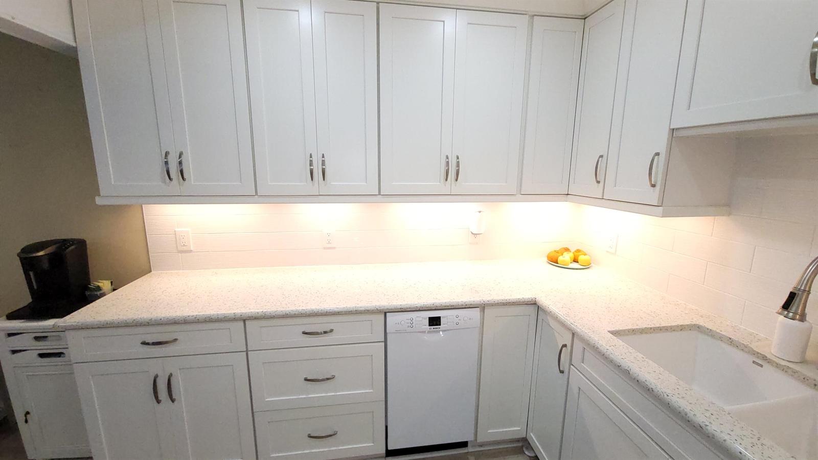 A kitchen features white cabinets, speckled countertops, a white dishwasher, and under-cabinet lighting — 34 Somerset B, West Palm Beach FL 33417, WEST PALM BEACH, FL