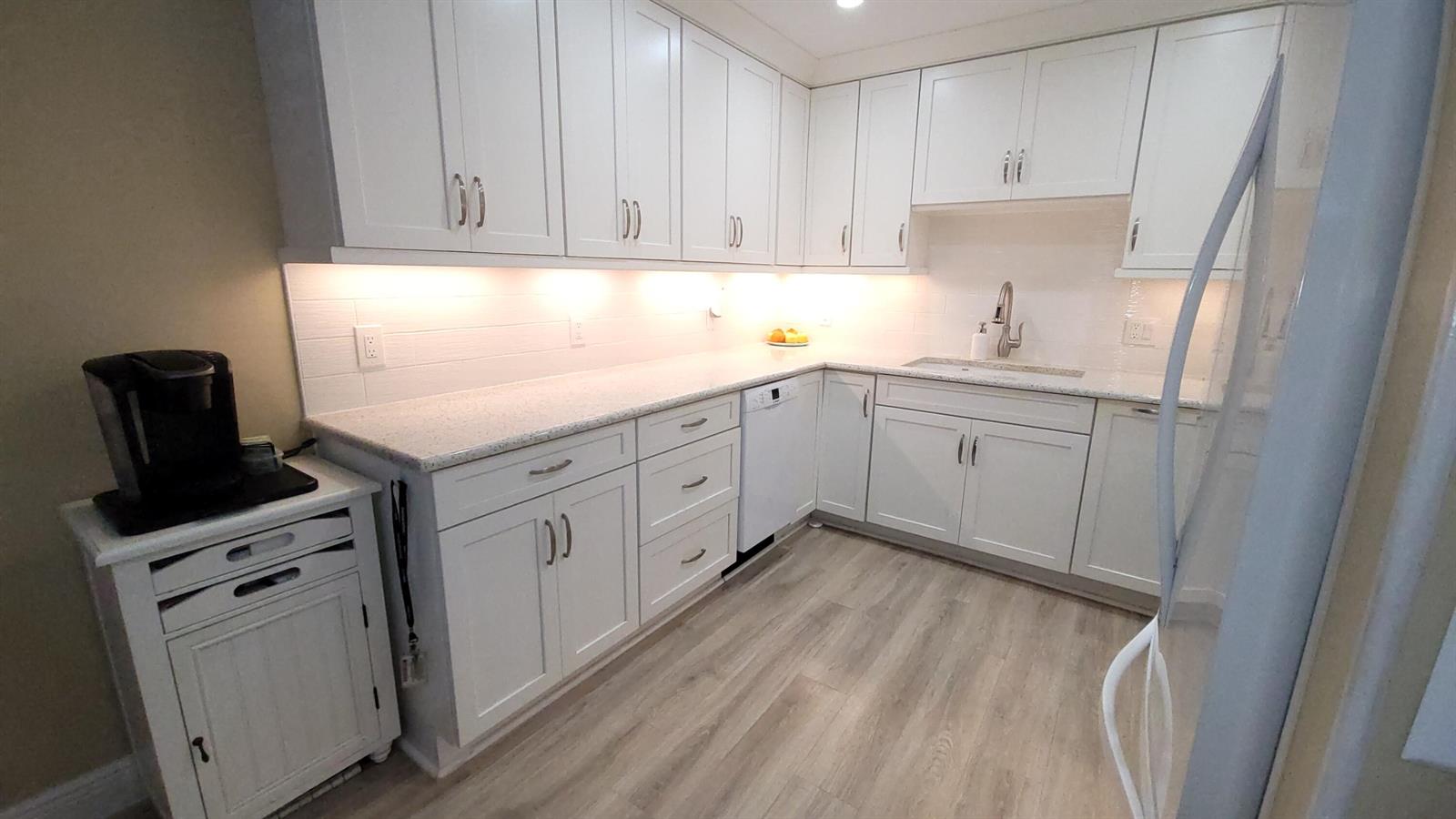 A kitchen features white cabinetry, light-colored countertops, a stainless steel sink, and wood-look flooring — 34 Somerset B, West Palm Beach FL 33417, WEST PALM BEACH, FL
