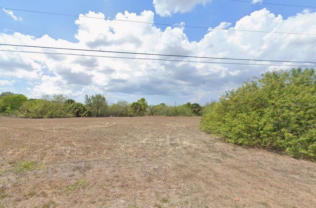A flat, grassy vacant lot is bordered by trees under a cloudy blue sky — 1218 NE 6TH AVENUE, CAPE CORAL, FL