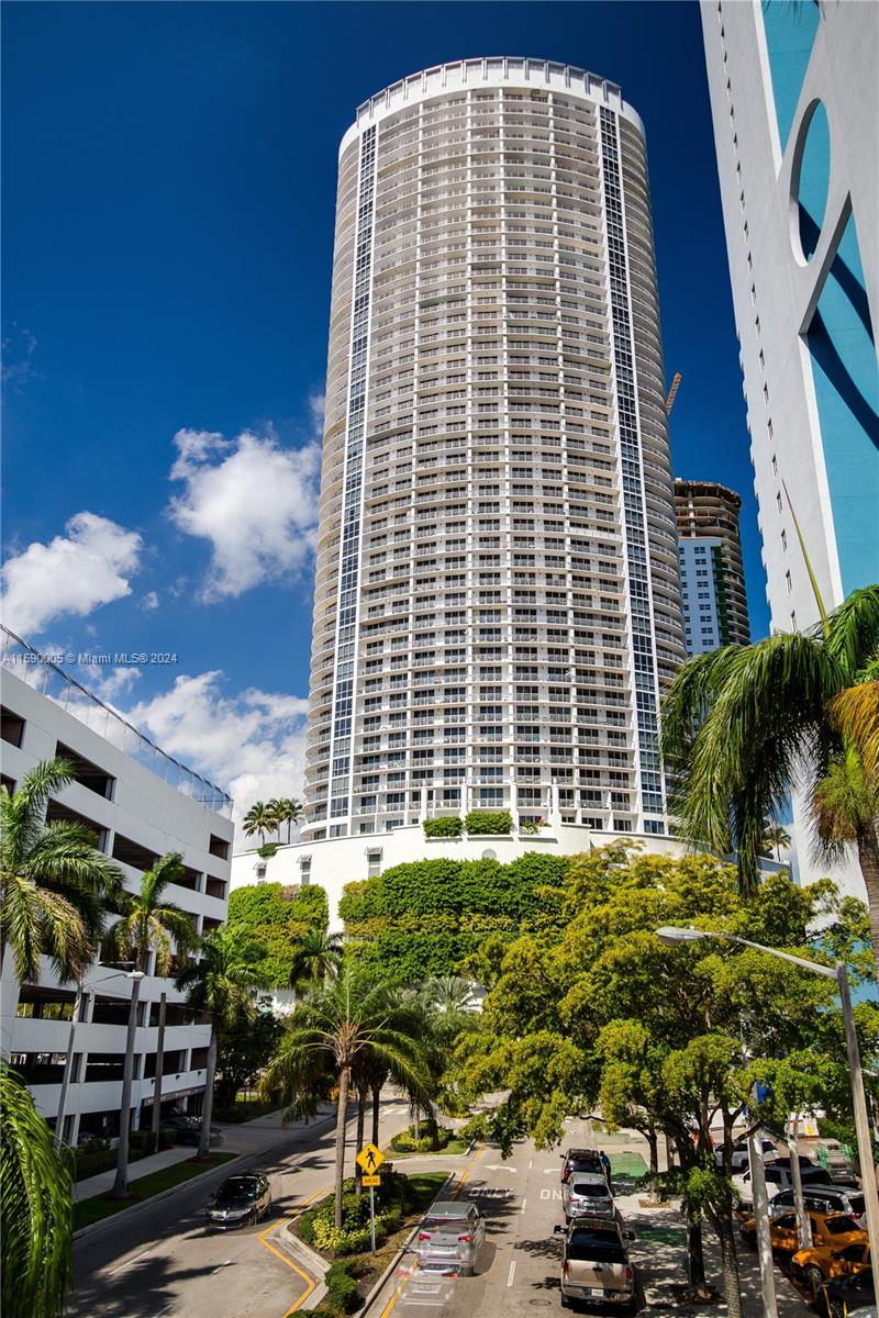 A tall, cylindrical residential skyscraper stands above a street with cars and lush green trees — 1750 N Bayshore Dr # 3512, Miami FL 33132, MIAMI, FL