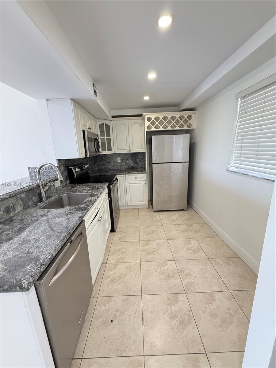 A kitchen features white cabinets, granite countertops, stainless steel appliances, and light-colored floor tiles — 14155 SW 87th St # E410, Miami FL 33183, MIAMI, FL