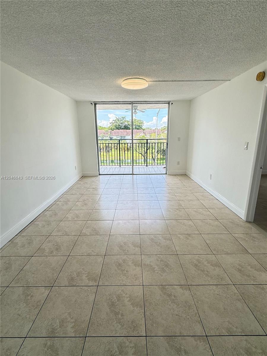 A living room with beige tile flooring, a textured ceiling, and a sliding glass balcony door — 14155 SW 87th St # E410, Miami FL 33183, MIAMI, FL