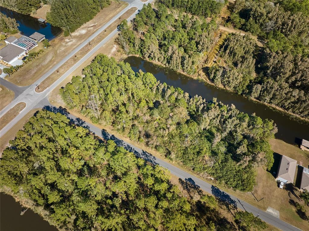 An aerial view shows a wooded residential lot situated between a road and a canal — 0 LANTANA DRIVE S, INDIAN LAKE ESTATES, FL