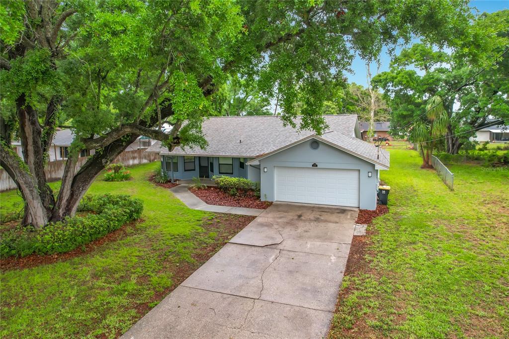 An exterior view of a single-story house with a concrete driveway and large shade trees — 109 SOUTH COURT, AUBURNDALE, FL
