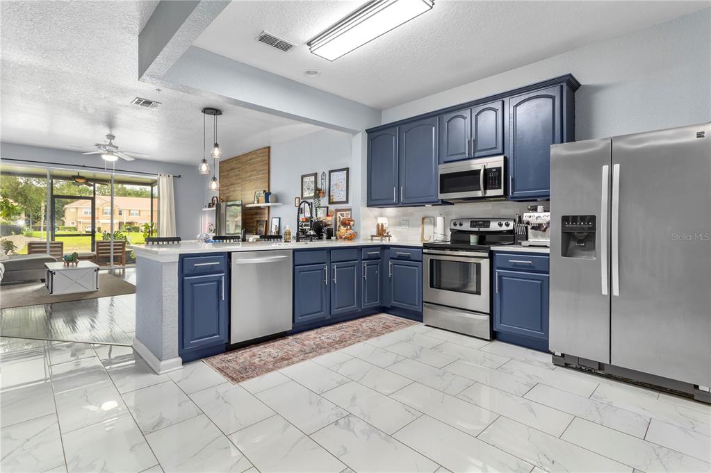 A kitchen with blue cabinets, stainless steel appliances, and white marble-look tile flooring — 3401 SHALLOT DRIVE UNIT 103, ORLANDO, FL