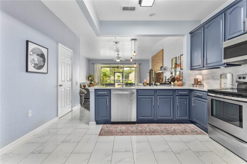 A kitchen with blue cabinets, stainless steel appliances, and white marble-look tile flooring — 3401 SHALLOT DRIVE UNIT 103, ORLANDO, FL