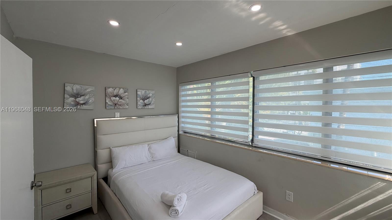 A bedroom features a white upholstered bed, a matching nightstand, and striped window shades — 10004 E Bay Harbor Dr # 10, Bay Harbor Islands FL 33154, BAY HARBOR ISLANDS, FL