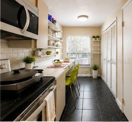 A narrow kitchen features a stove, open shelving, a breakfast bar with chairs, and tile flooring — 4704 JASMINE CREEK LANE UNIT 1508A, ORLANDO, FL