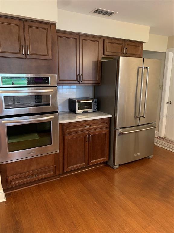 A kitchen features dark wood cabinets, stainless steel appliances, and a white subway tile backsplash — 1501 INDIANA AVENUE, PALM HARBOR, FL