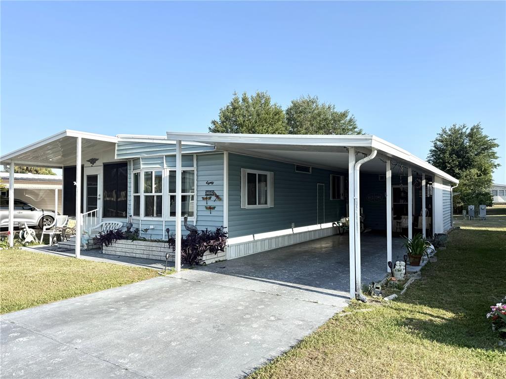 A light blue mobile home features a large carport and a front porch area — 34642 SWEETPEA LANE LANE, ZEPHYRHILLS, FL